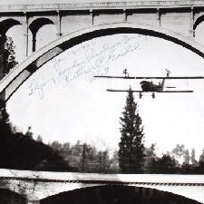 The black and white shot of a plane flying under a bridge